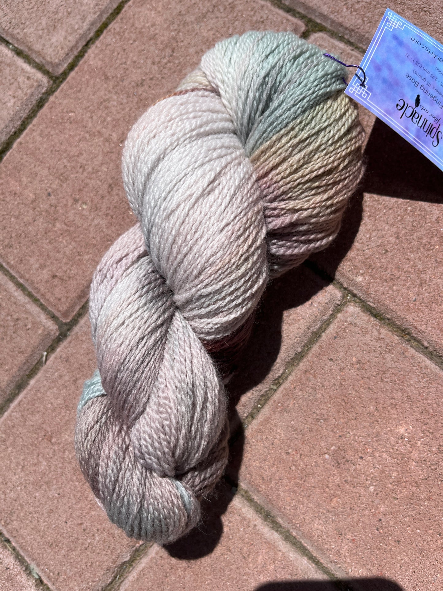 Skein of soft, multi-colored yarn with pastel shades on brick pavement in natural light