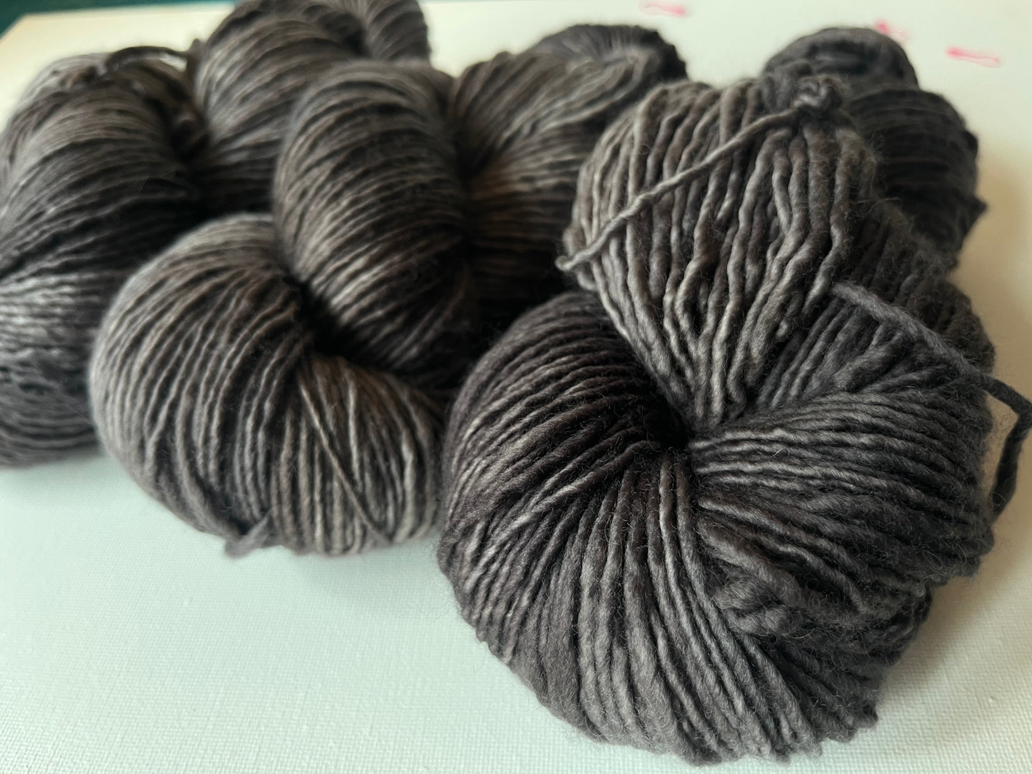 Close-up of multiple skeins of charcoal gray wool yarn on a light surface, soft texture