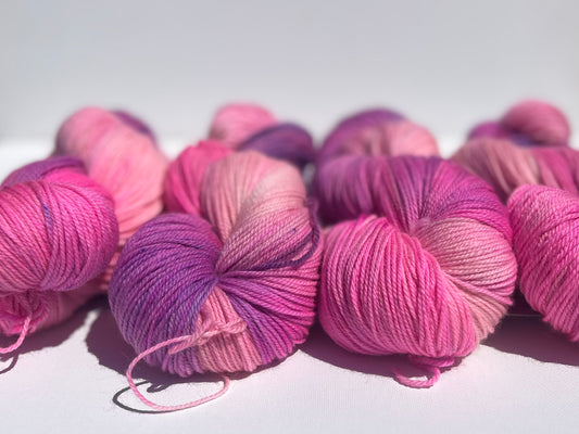 Skeins of hand-dyed yarn in vibrant shades of pink and purple on white background