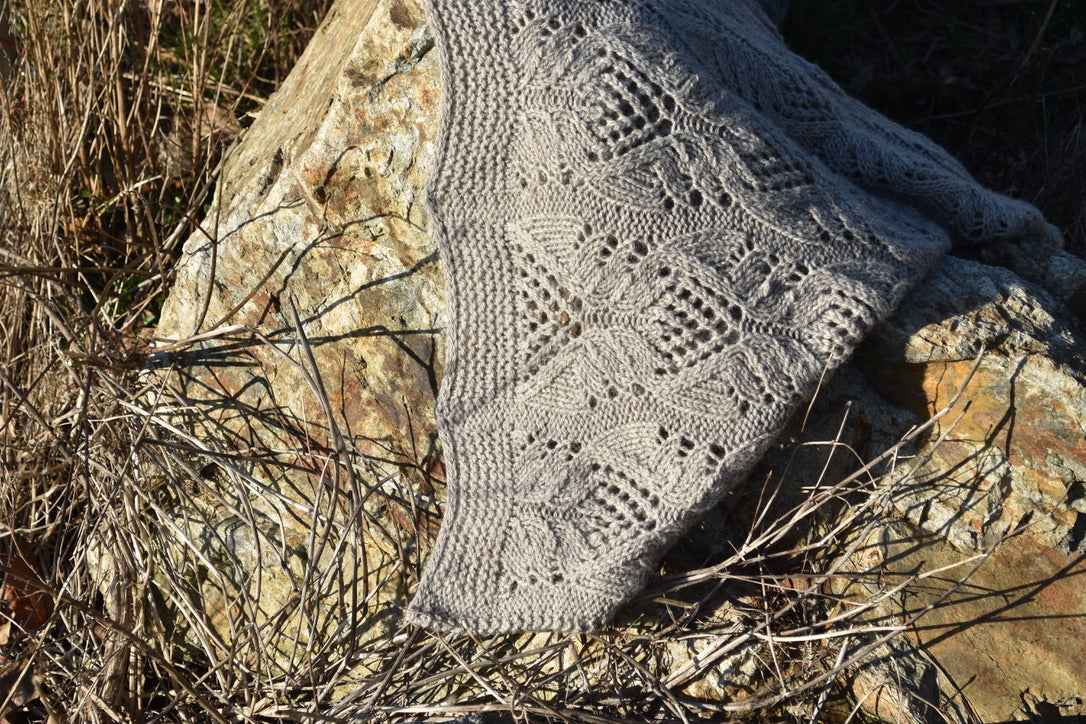 Beige knitted lace shawl with intricate patterns draped over a large rock outdoors