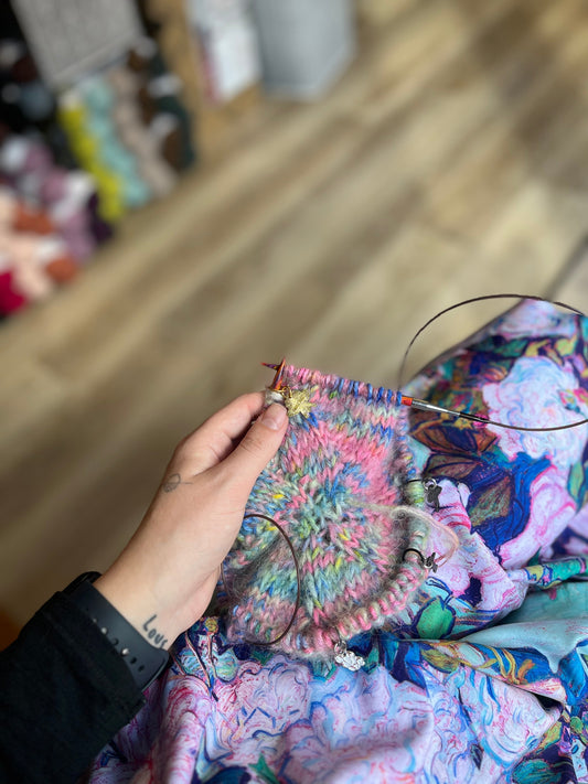 Hand knitting colorful pink and blue circular pattern with metal circular needles on floral fabric background
