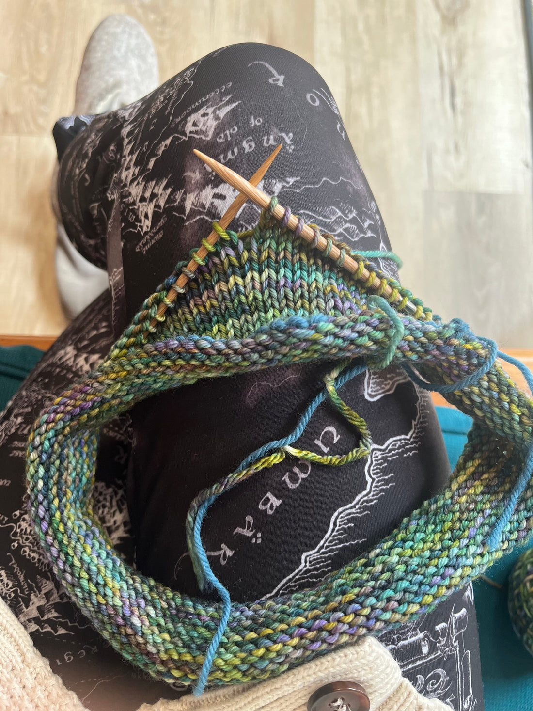 Close-up of colorful yarn knitting with wooden needles on lap covered by black map-patterned leggings