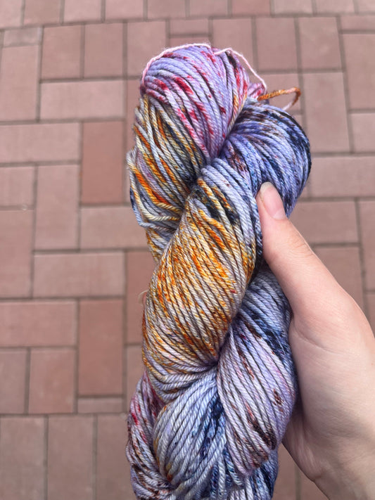 Hand holding skein of multicolored variegated yarn with purple, orange, yellow, and blue speckles