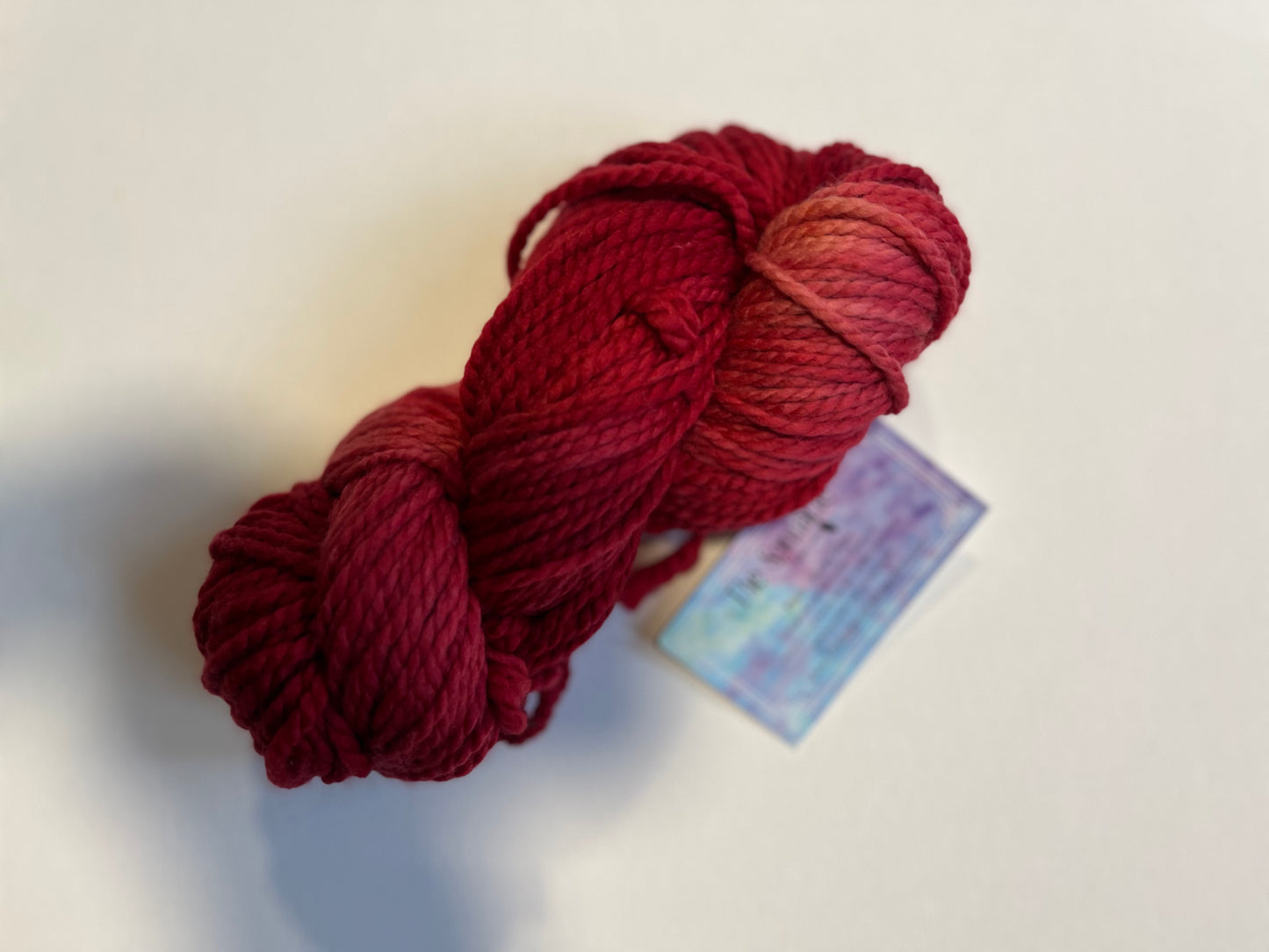 Skein of thick red and dark pink yarn on white surface with blurred label