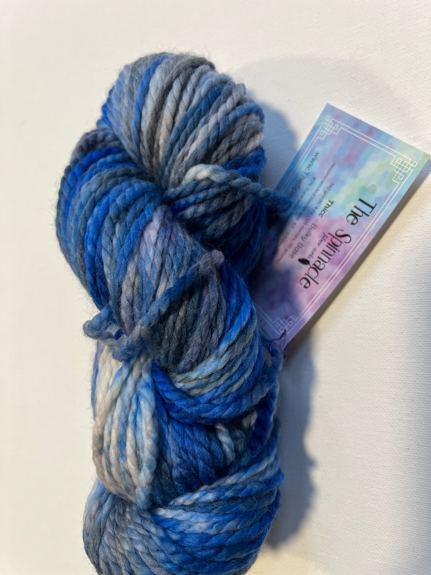 Skein of hand-dyed variegated blue and gray chunky yarn with The Spinnacle label