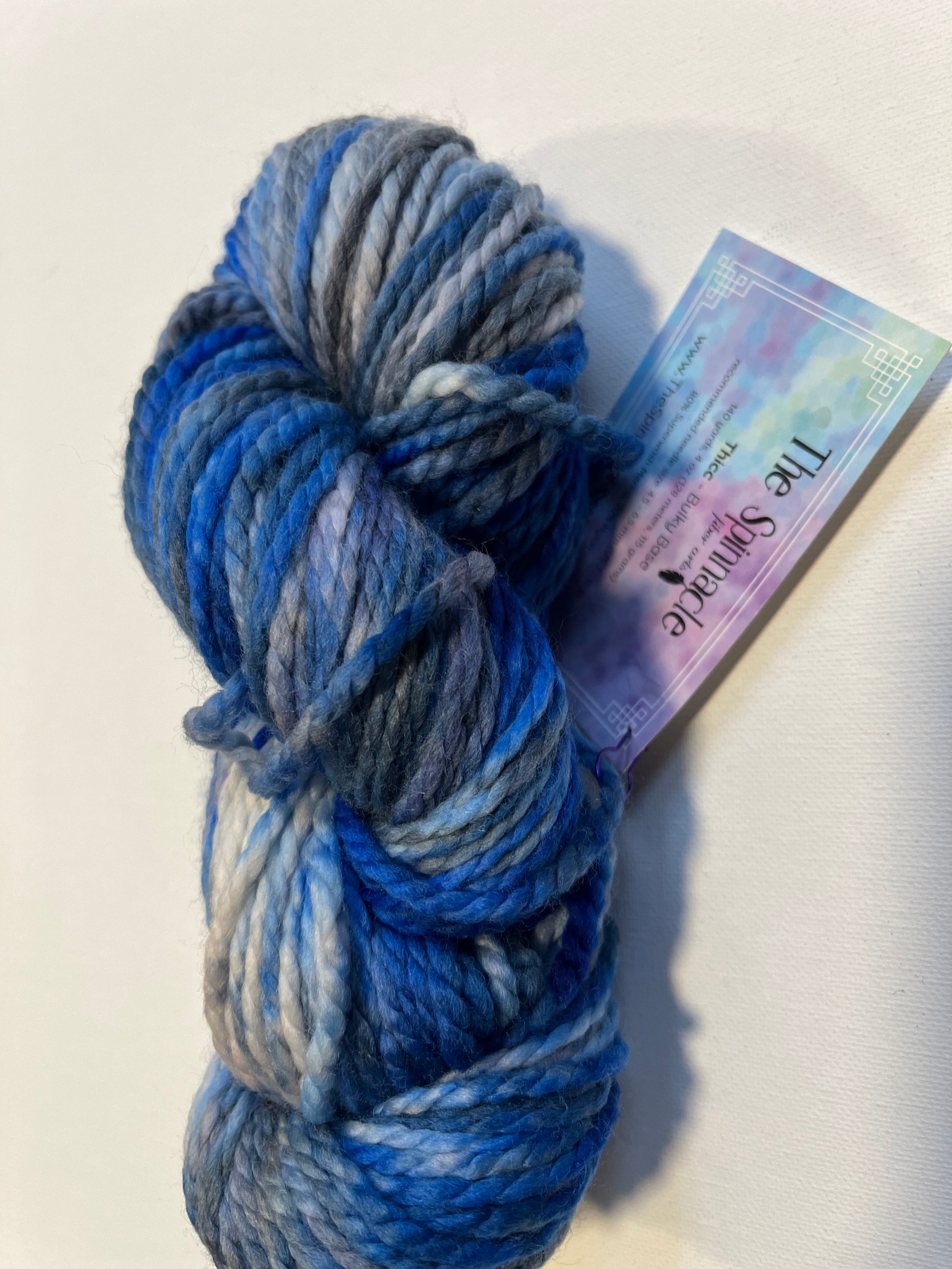 Skein of hand-dyed variegated blue and gray chunky yarn with The Spinnacle label