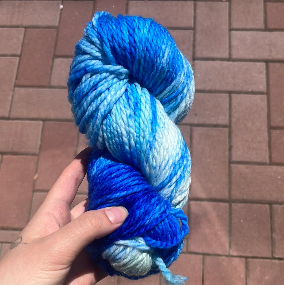 hand holding a skein of blue gradient yarn on brick pavement background