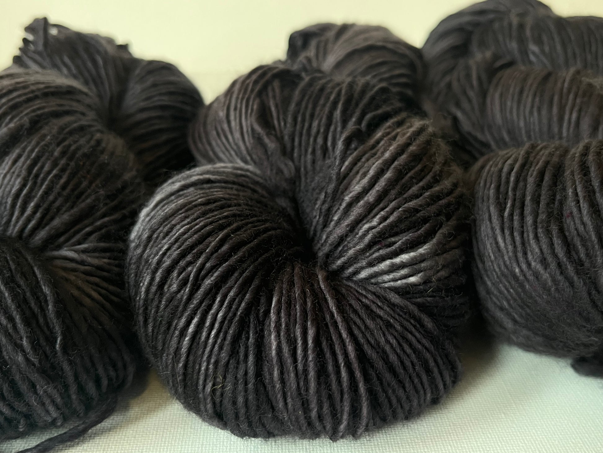Close-up of dark gray hand-spun wool yarn skeins on light fabric background