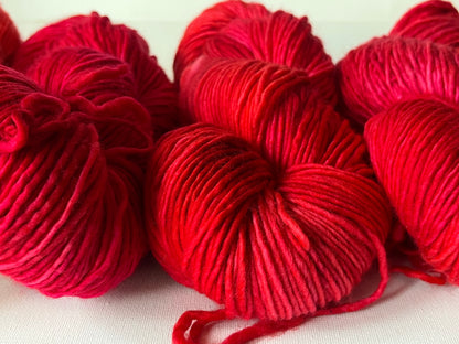 Close-up of vibrant red yarn skeins on white fabric, showing soft wool texture