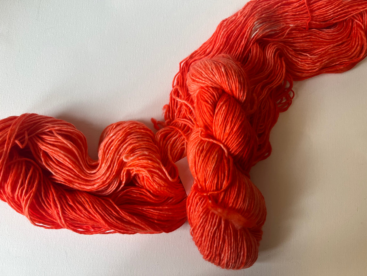 Bright red-orange skein and loosely arranged yarn on a white textured surface