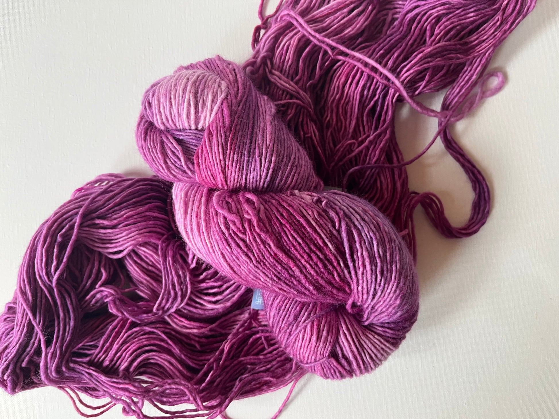 Hand-dyed skein of variegated pink and purple yarn on white background