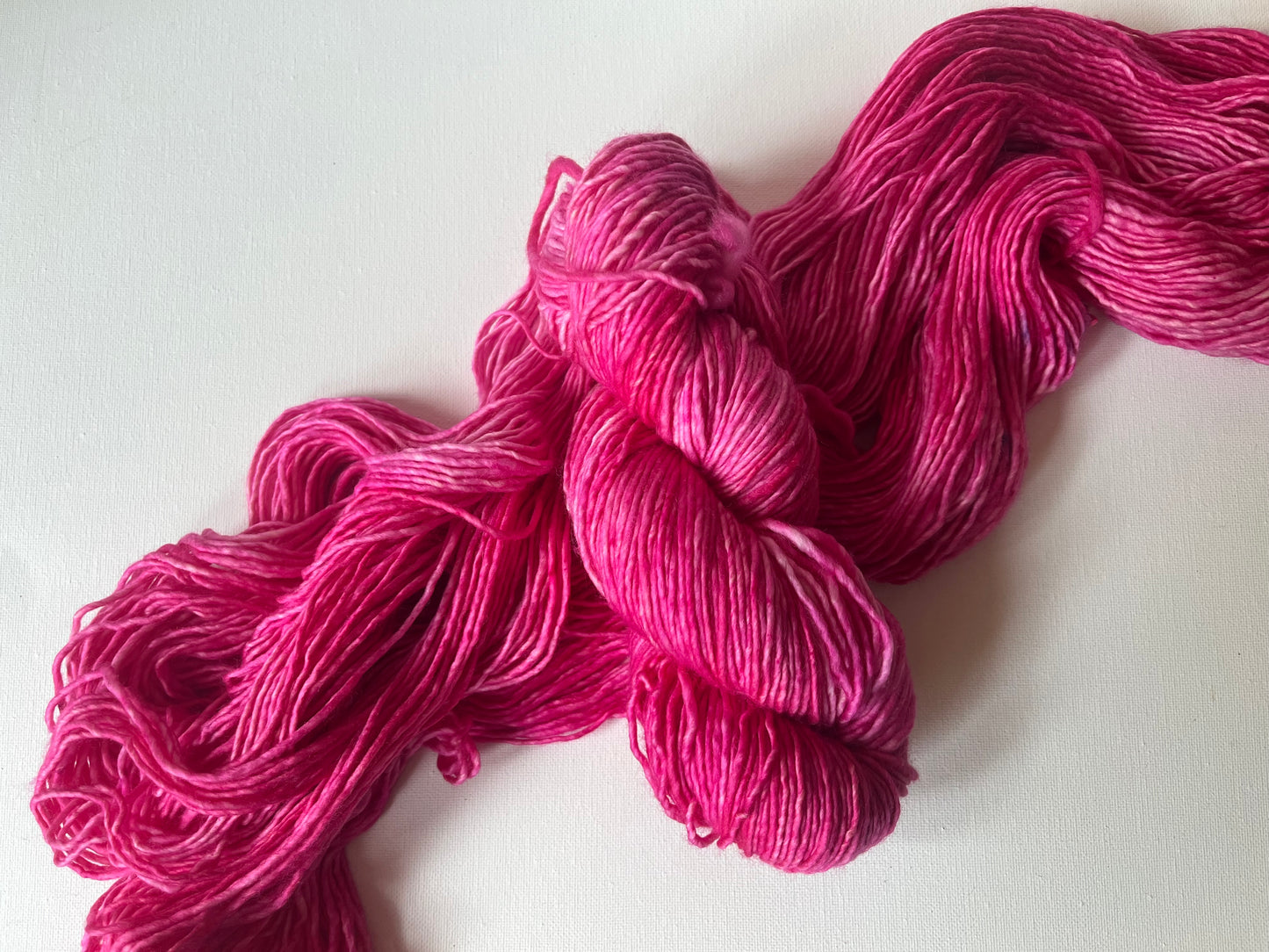 Bright pink hand-dyed yarn skein on white background, soft wool knitting material