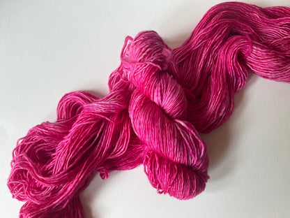 Bright pink hand-dyed yarn skein on white background, soft wool knitting material
