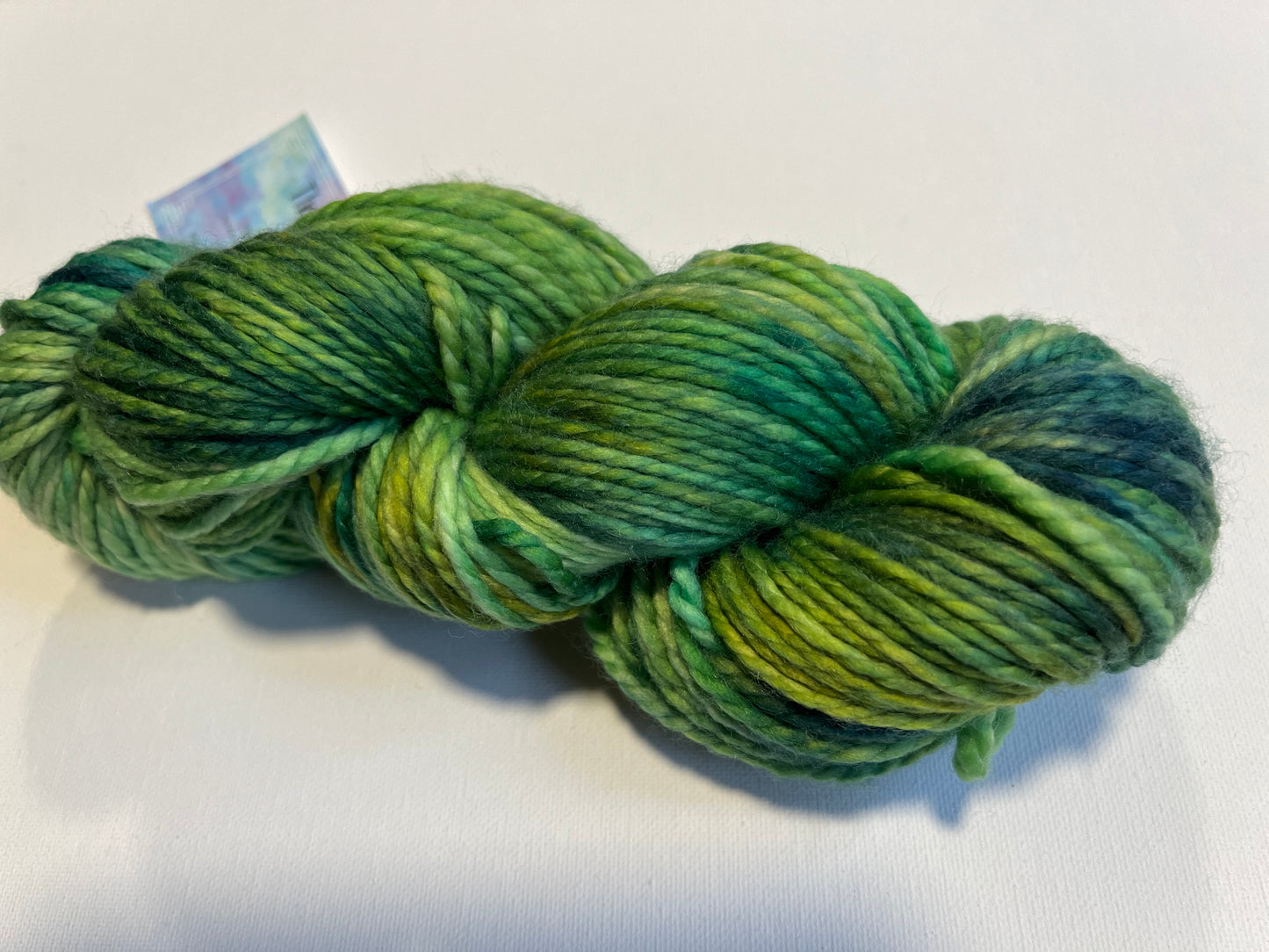 Skein of variegated green and teal wool yarn on white background for knitting and crocheting
