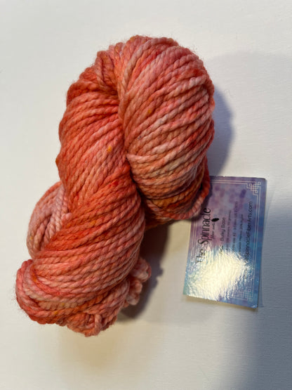 Hand-dyed bulky yarn skein in shades of pink and orange with label from The Spinnacle Fiber Arts