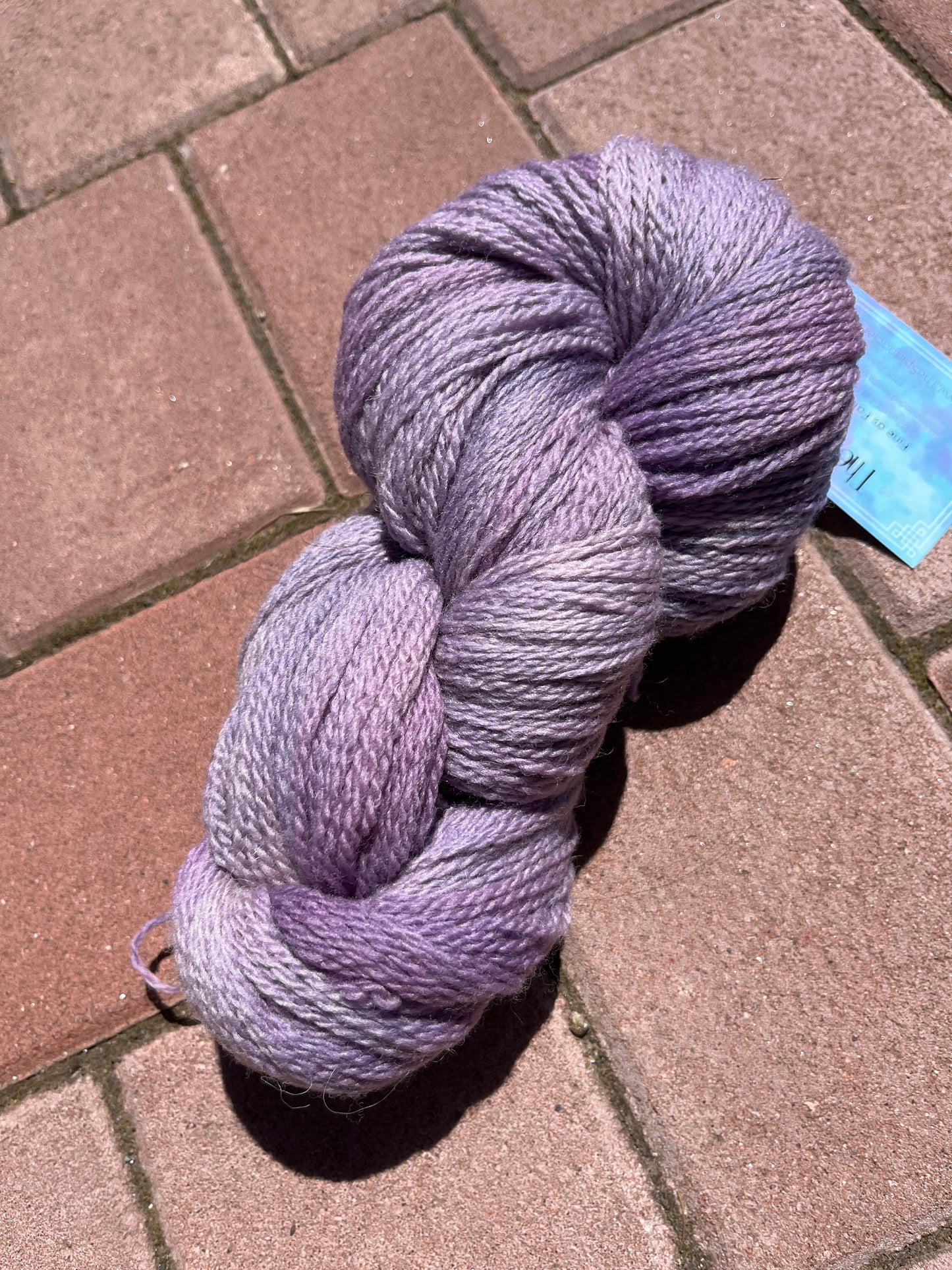 Skein of soft purple gradient yarn on a sunlit red brick pavement