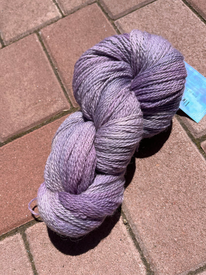 Skein of soft purple gradient yarn on a sunlit red brick pavement
