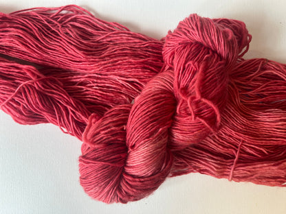 Hand-dyed red yarn skeins and loose strands on a white background