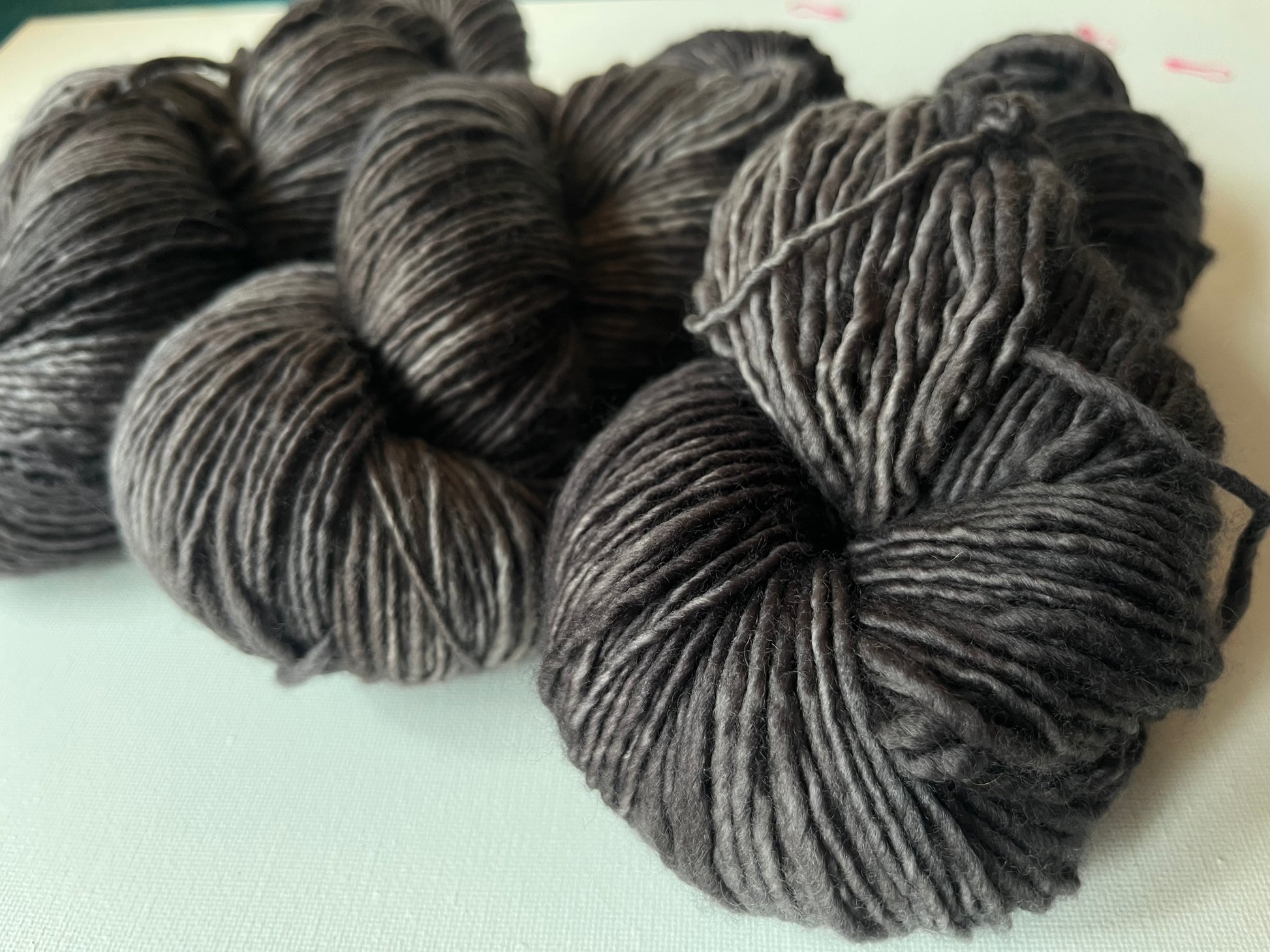 Close-up of multiple skeins of charcoal gray wool yarn on a light surface, soft texture