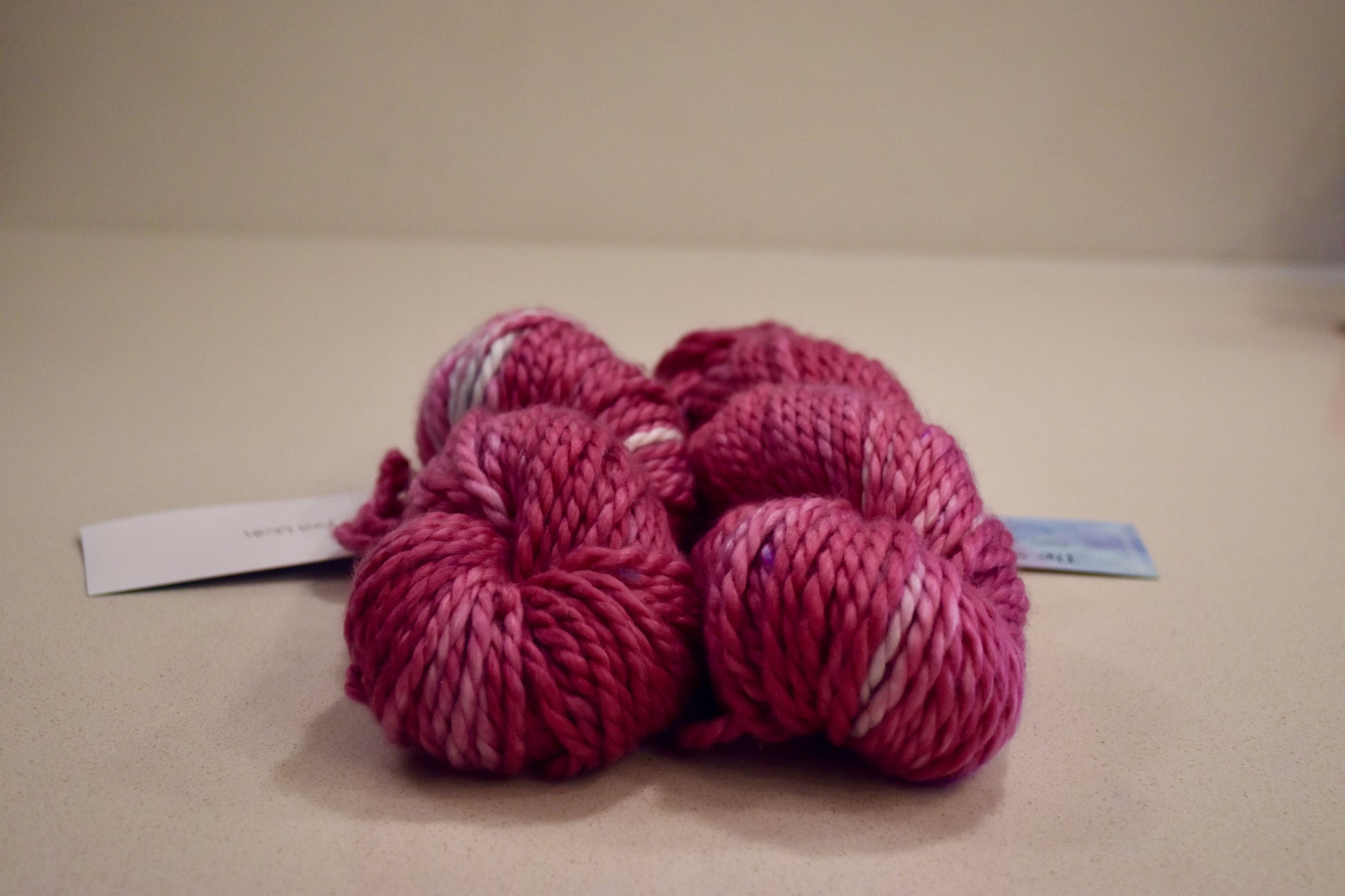 Two skeins of thick pink and purple variegated yarn on a beige surface