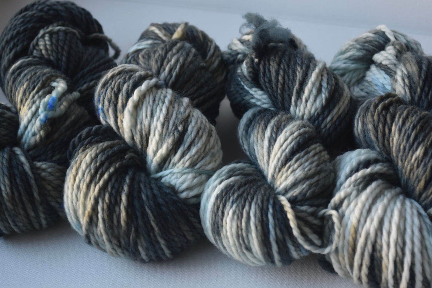 Close-up of four skeins of thick variegated yarn in shades of blue, gray, and white on a plain surface