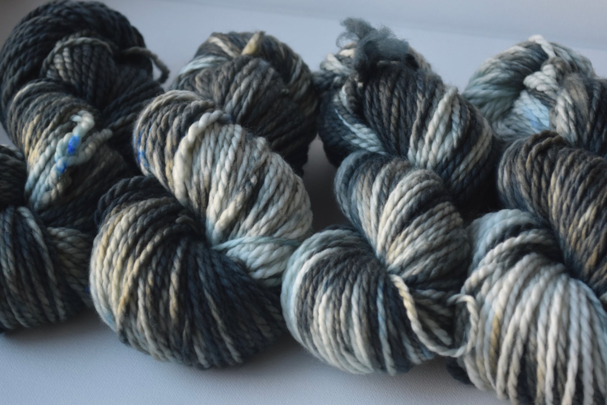 Close-up of four skeins of thick variegated yarn in shades of blue, gray, and white on a plain surface