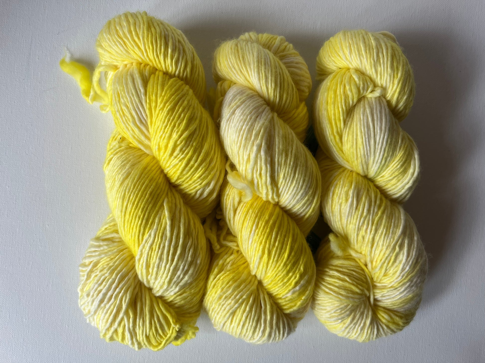 Three skeins of yellow and white variegated yarn on a white background
