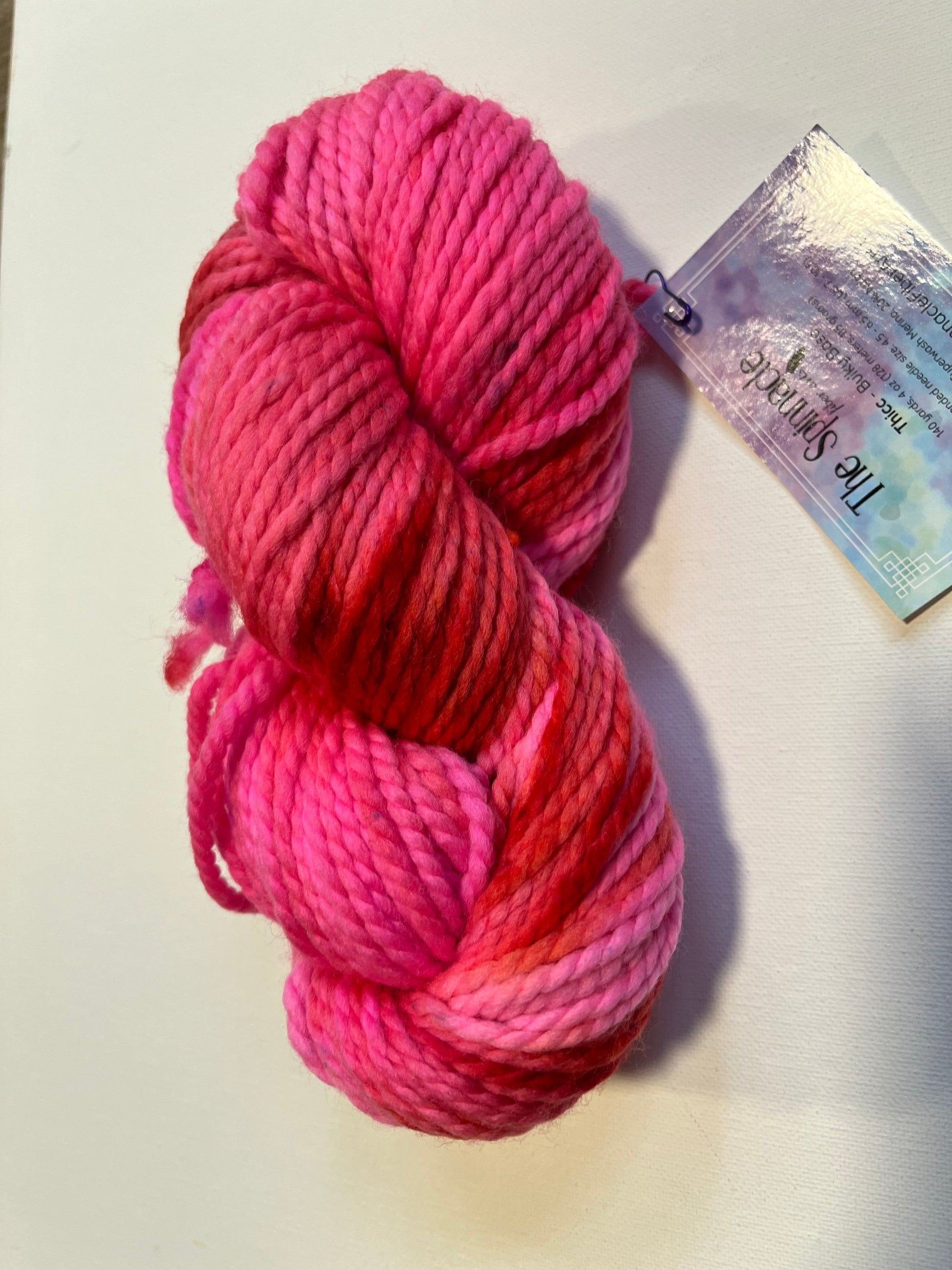 Skein of vibrant pink and red variegated yarn with a product label on white background