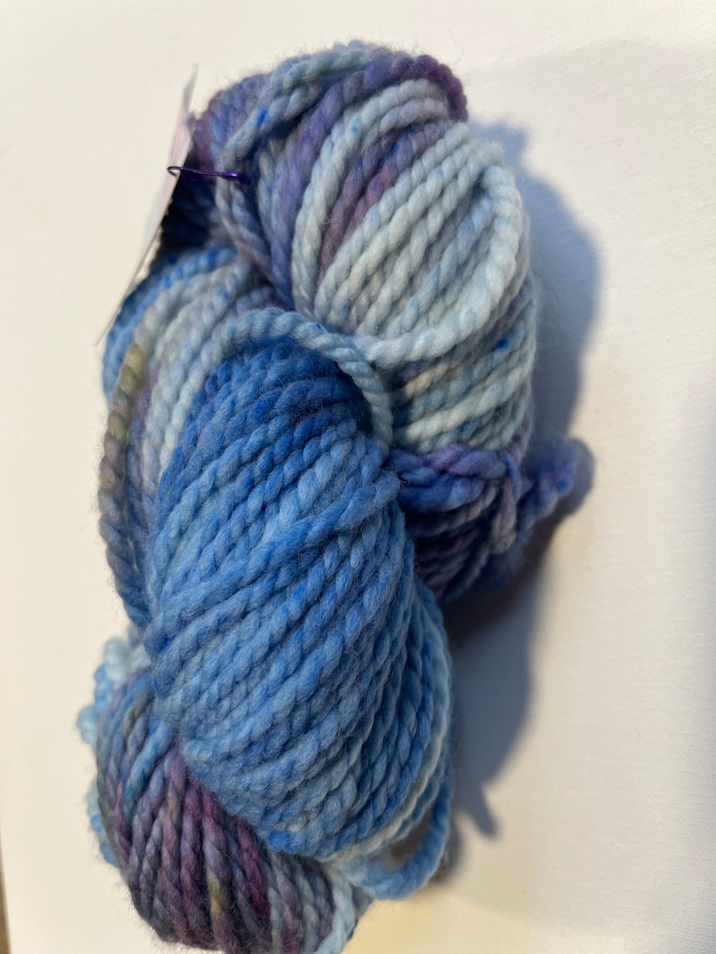 Thick variegated yarn skein in shades of blue and purple on a white background