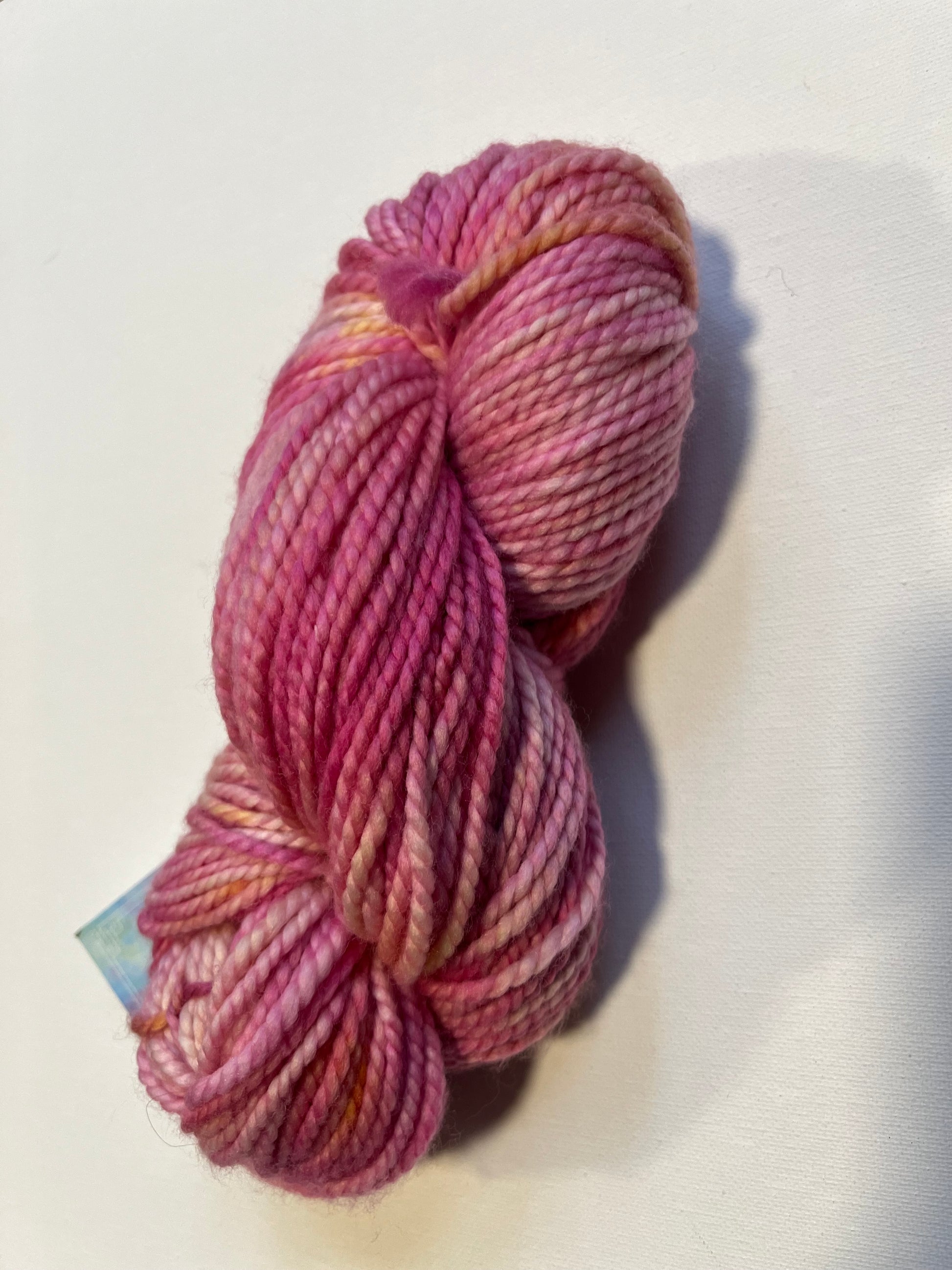 Skein of variegated pink and peach hand-dyed yarn on white background