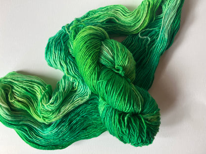 Skein of hand-dyed variegated green yarn on a white surface, showing rich color gradients