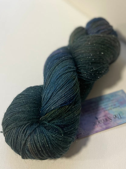 skein of dark blue and green speckled yarn with metallic threads on white surface