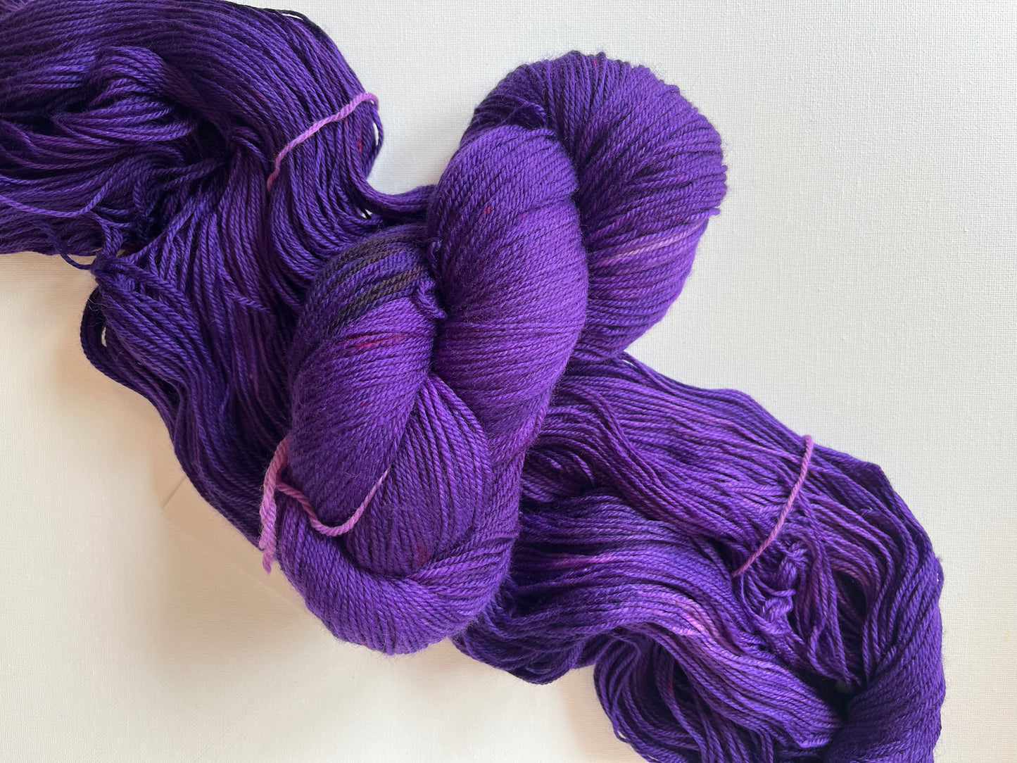 Two skeins of rich purple yarn with subtle lighter highlights on a white background