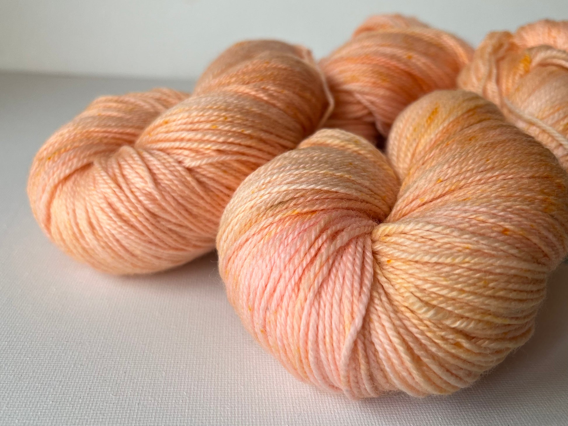 Close-up of soft, hand-dyed peach and cream yarn skeins on a white background