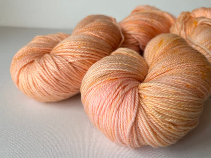 Close-up of soft, hand-dyed peach and cream yarn skeins on a white background
