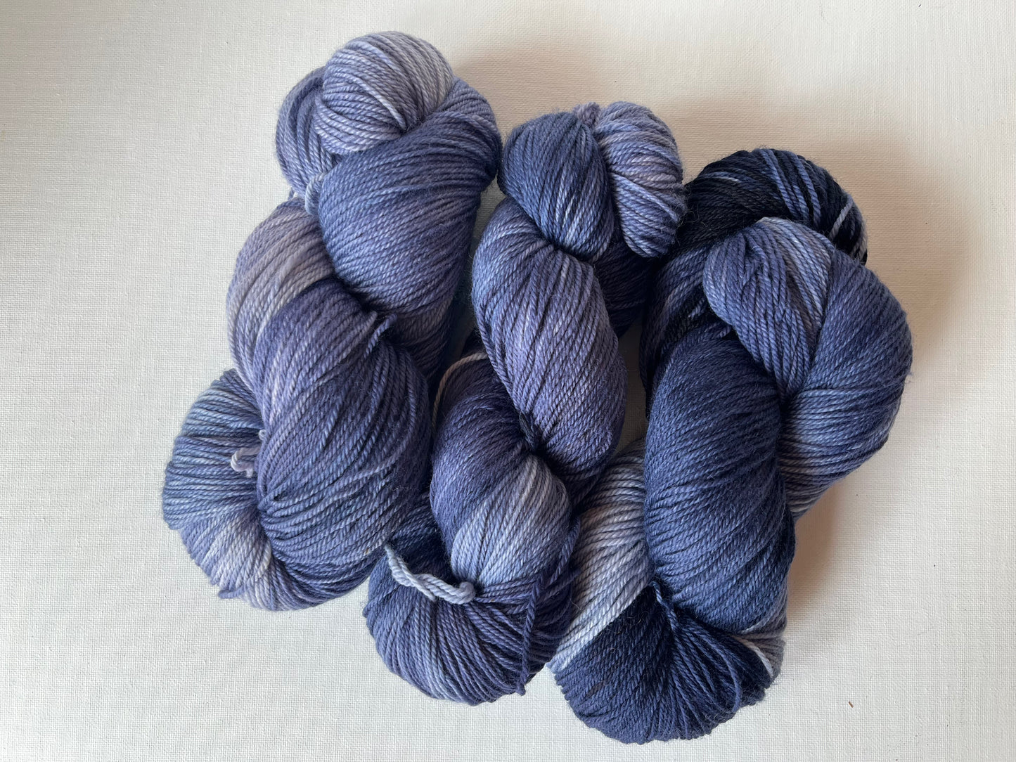 Three skeins of variegated blue and purple yarn on white fabric background