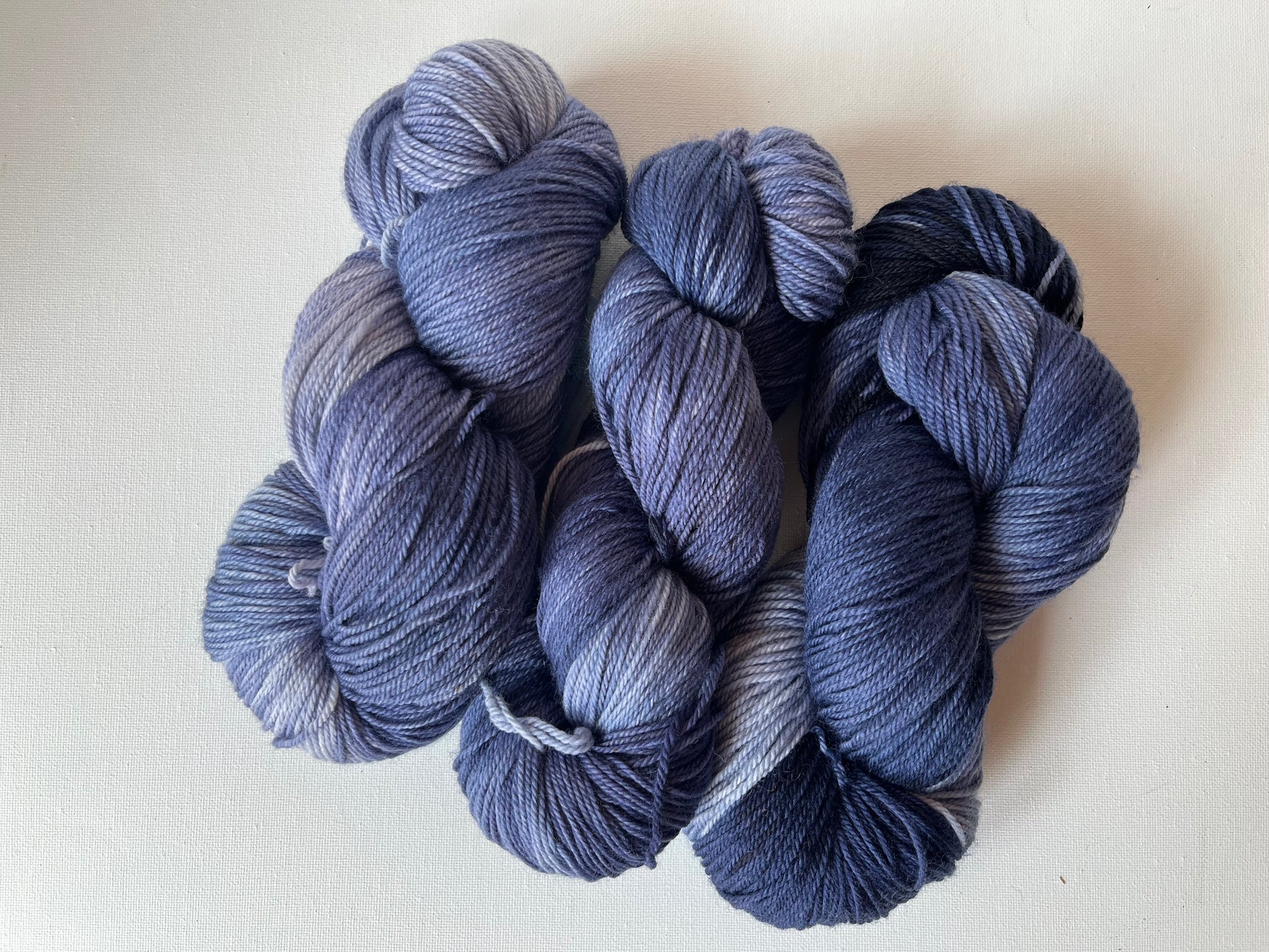 Three skeins of variegated blue and purple yarn on white fabric background