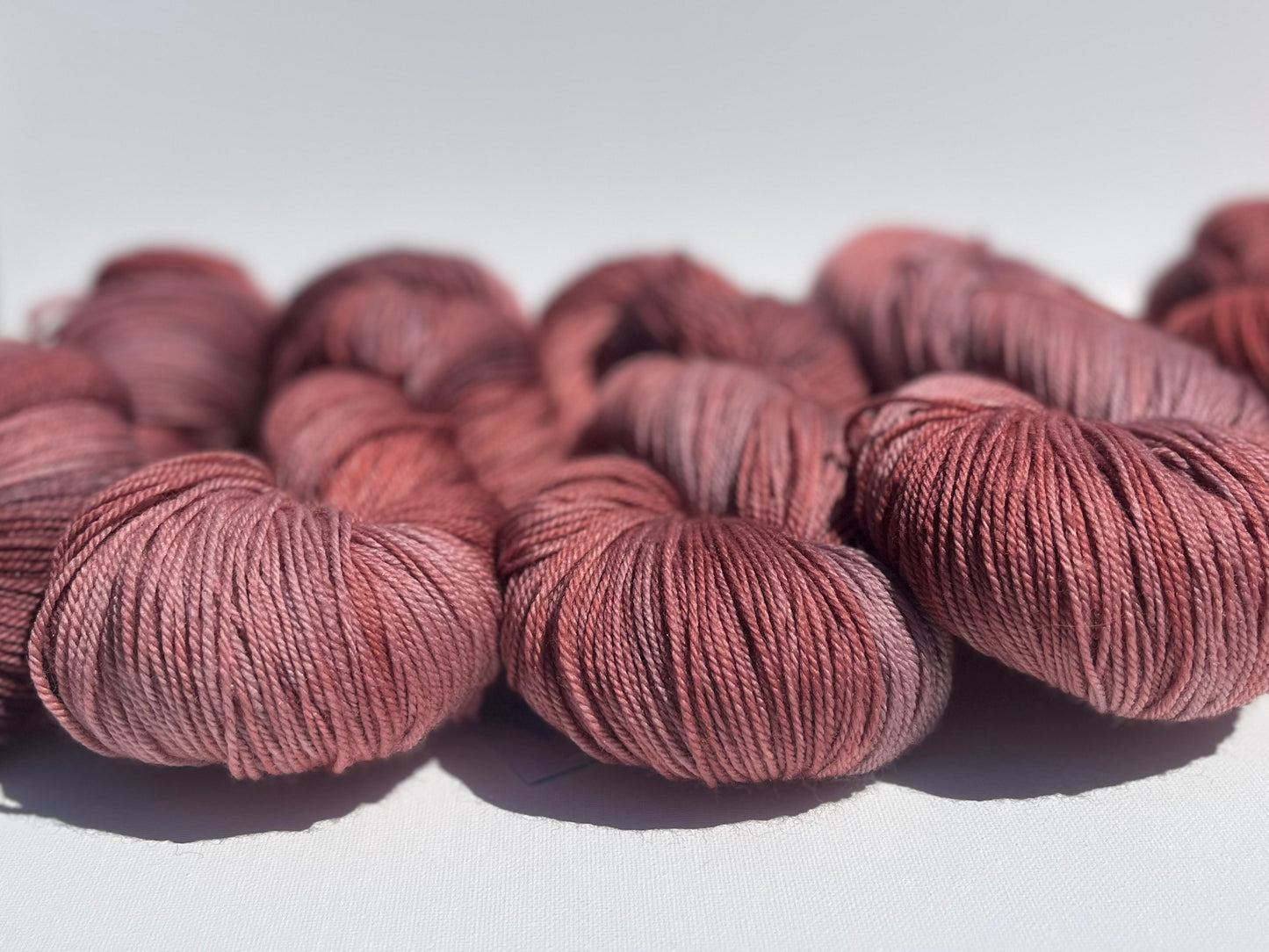 Multiple skeins of soft dusty rose pink yarn on a white surface, close-up view