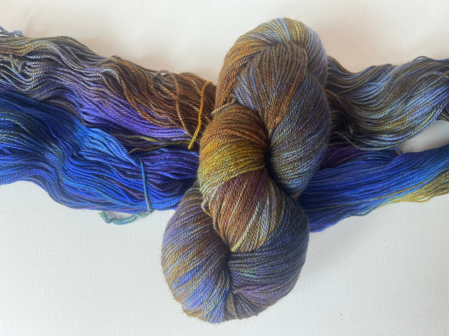 Skein of multicolored yarn in blue, purple, gold, and brown shades on white background