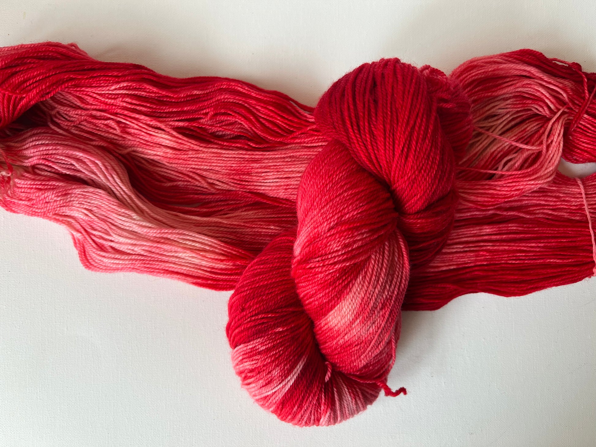 Hand-dyed gradient yarn skein in shades of red and pink on white background