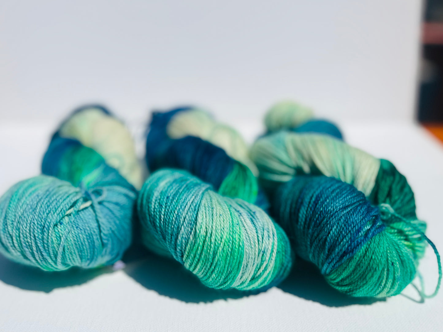 Six skeins of variegated yarn in shades of teal, green, and blue on a white surface