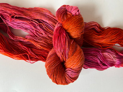 skein of hand-dyed yarn in shades of orange, pink, and red on white background