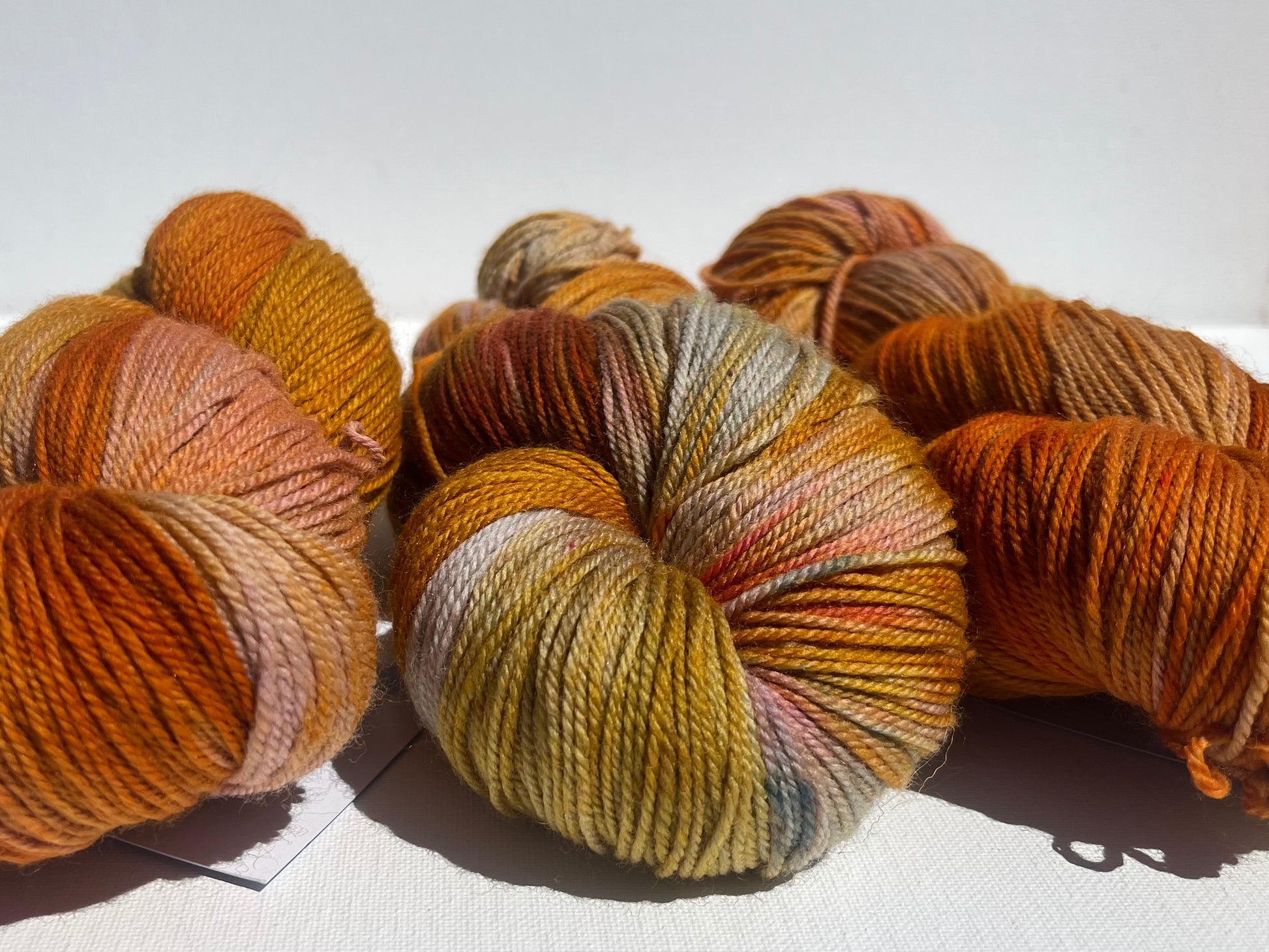 Three skeins of variegated yarn in warm autumn colors including orange, gold, and brown on white background