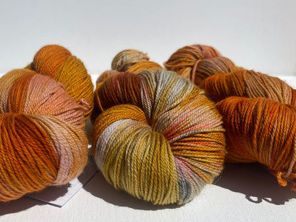 Three skeins of variegated yarn in warm autumn colors including orange, gold, and brown on white background