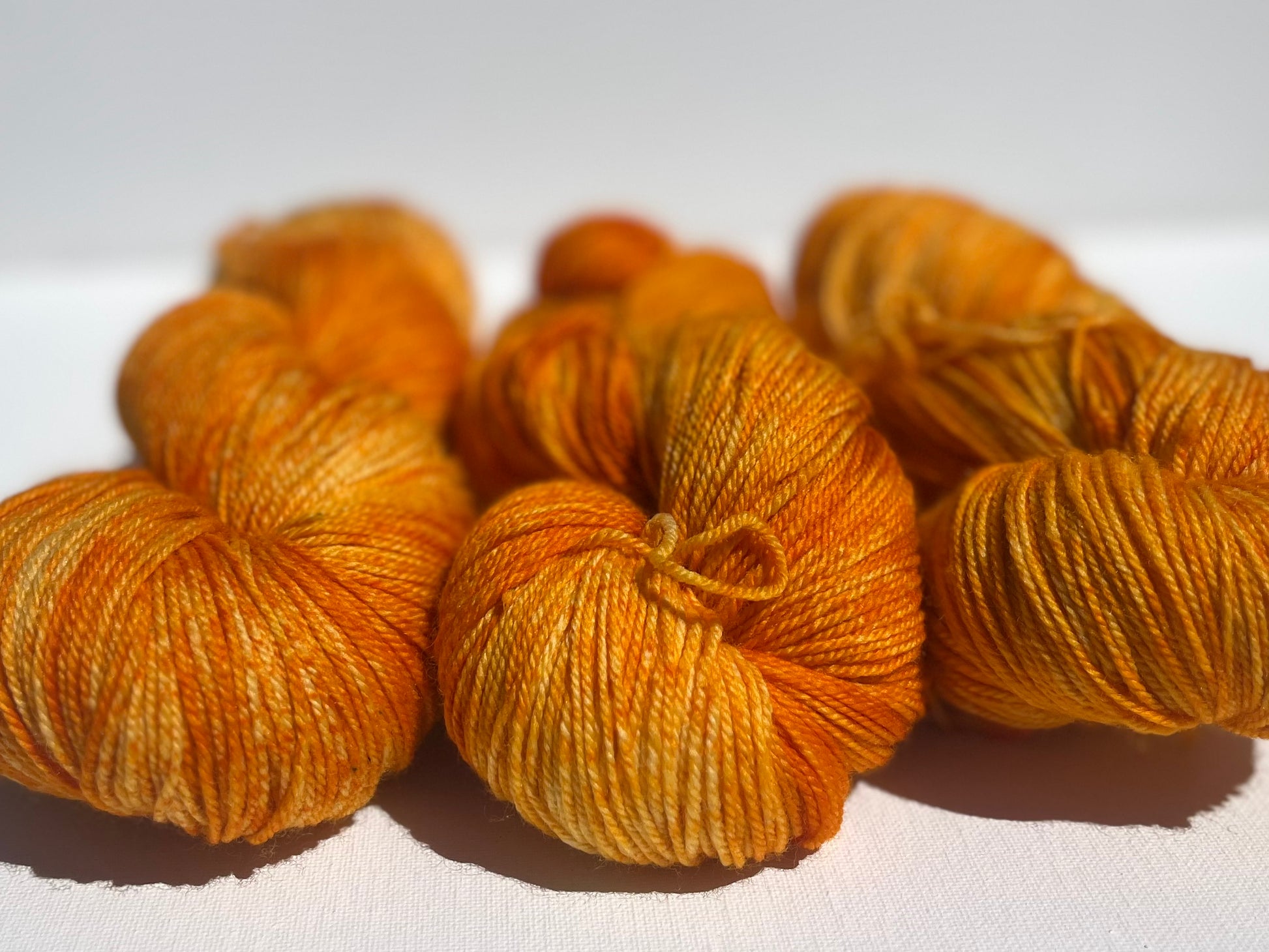 Close-up of three skeins of hand-dyed orange yarn on white surface