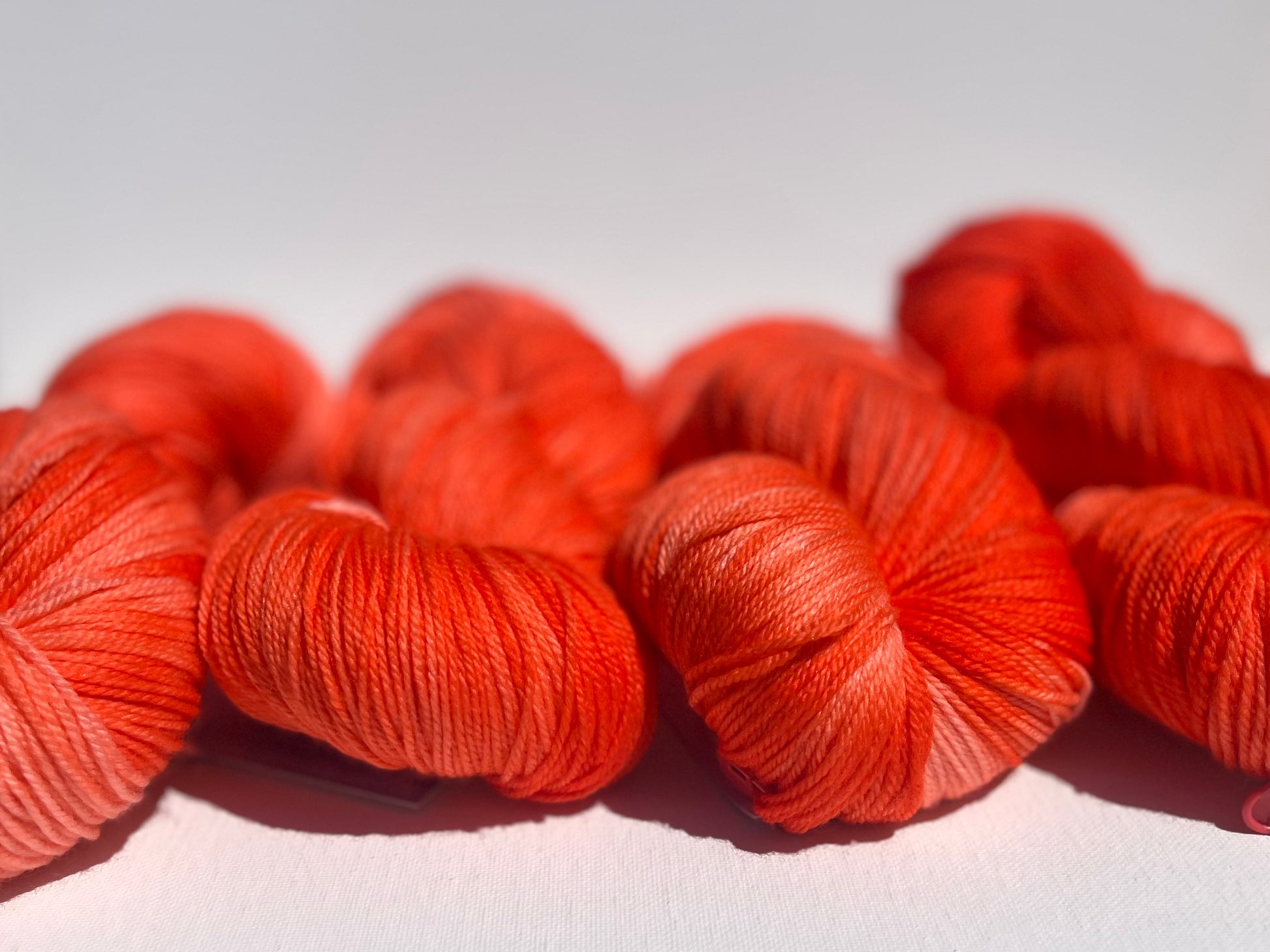 Four skeins of vibrant orange yarn on a white surface with a soft gradient background