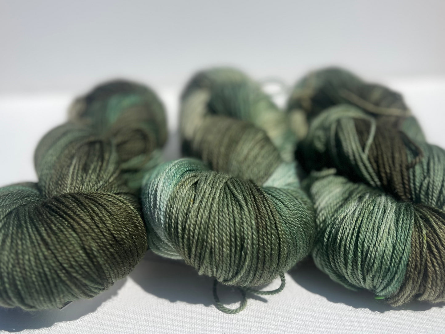Three skeins of green variegated yarn with shades of olive and mint on a white surface