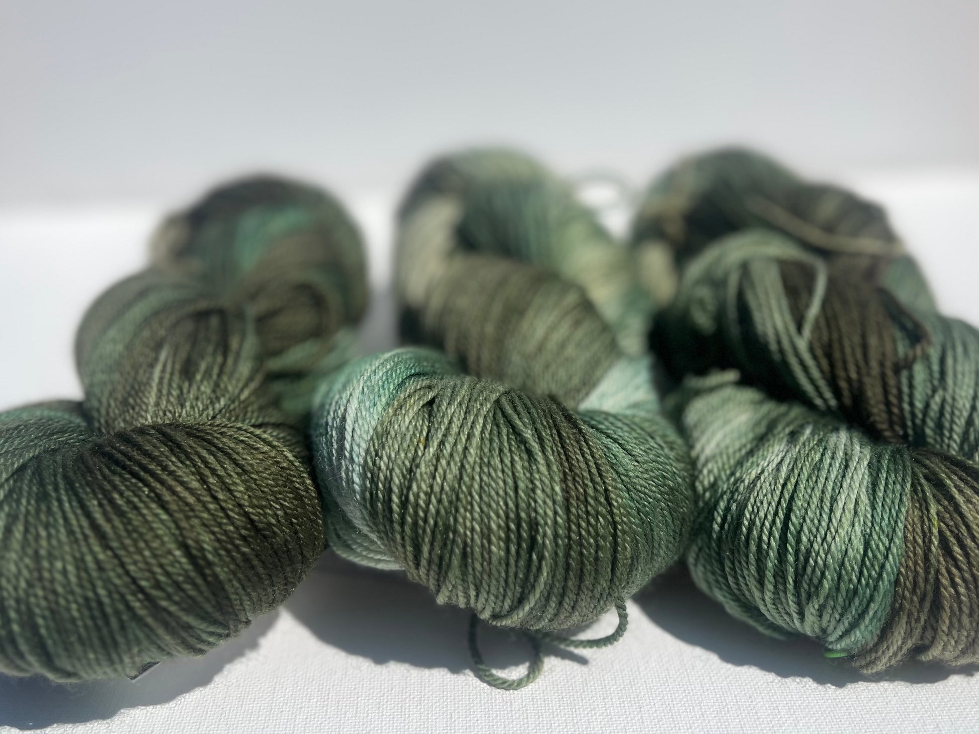 Three skeins of green variegated yarn with shades of olive and mint on a white surface
