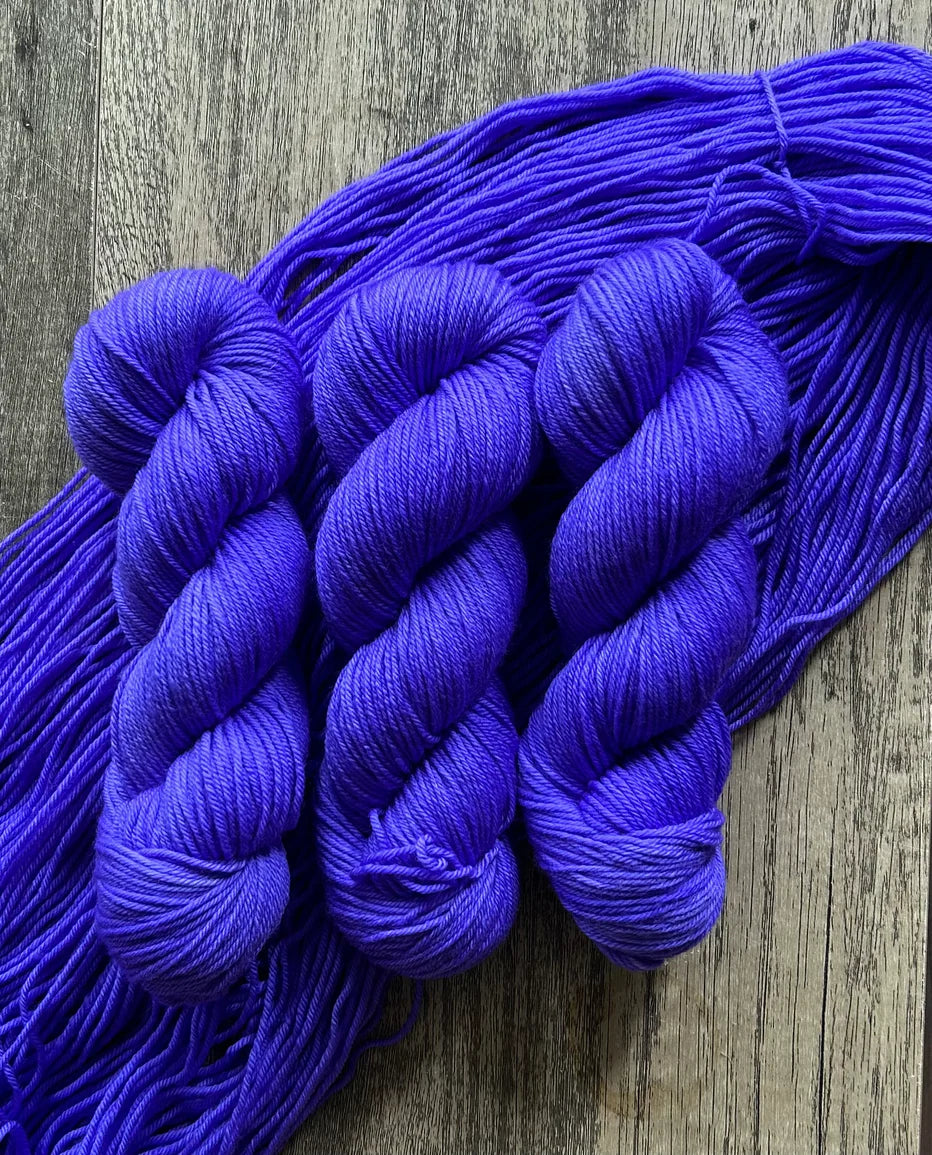 Three skeins of vibrant purple yarn on rustic wooden surface with loose strands