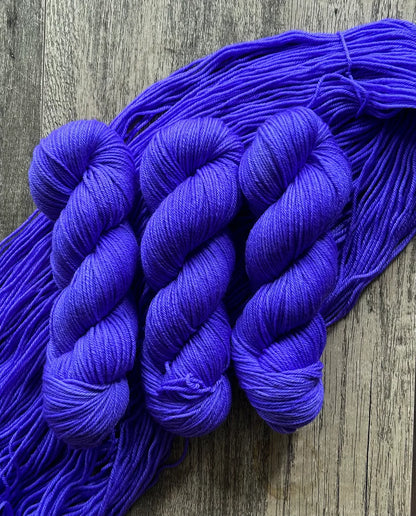 Three skeins of vibrant purple yarn on rustic wooden surface with loose strands